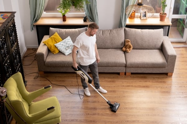 young-man-casualwear-doing-domestic-work-while-cleaning-floor-living-room-with-vacuum-cleaner-armchair-couch